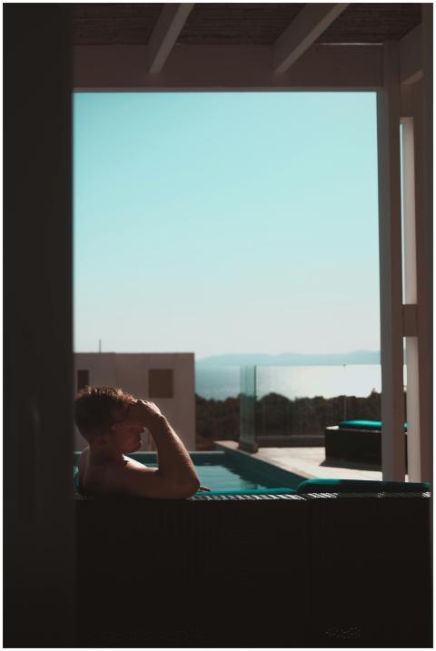 Man relaxing at an outdoor pool with a scenic ocea