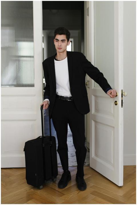 Elegant young man in suit holding luggage enters a