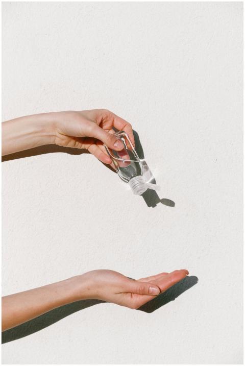 Person applying hand sanitizer against white backd