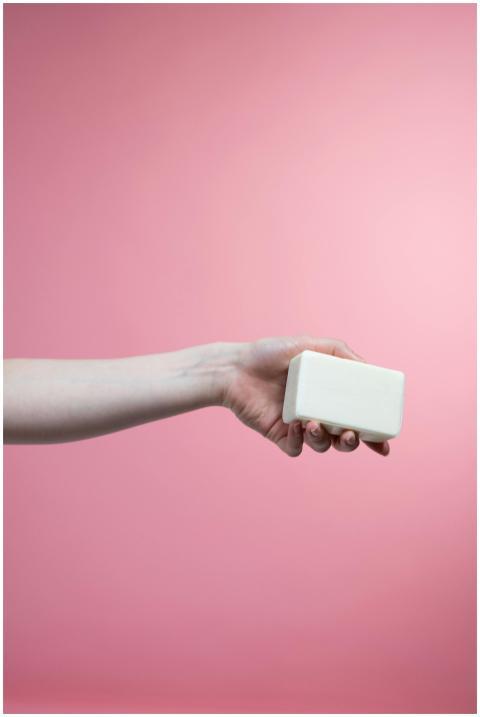 A hand holding a bar of soap with a pink backgroun