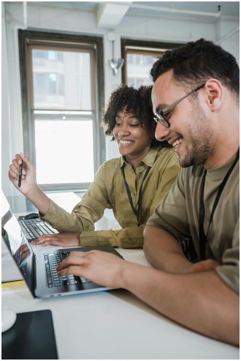 Two colleagues happily working on laptops together