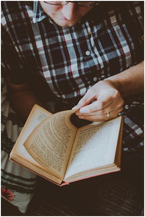 Adult male wearing plaid shirt reading a book indo