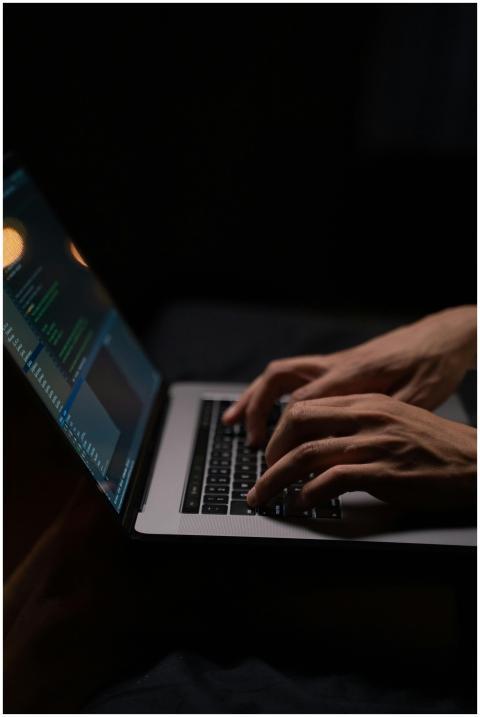 Hands typing code on a laptop keyboard in a dark r