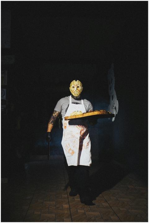A man in a horror mask and apron serves pizza in e