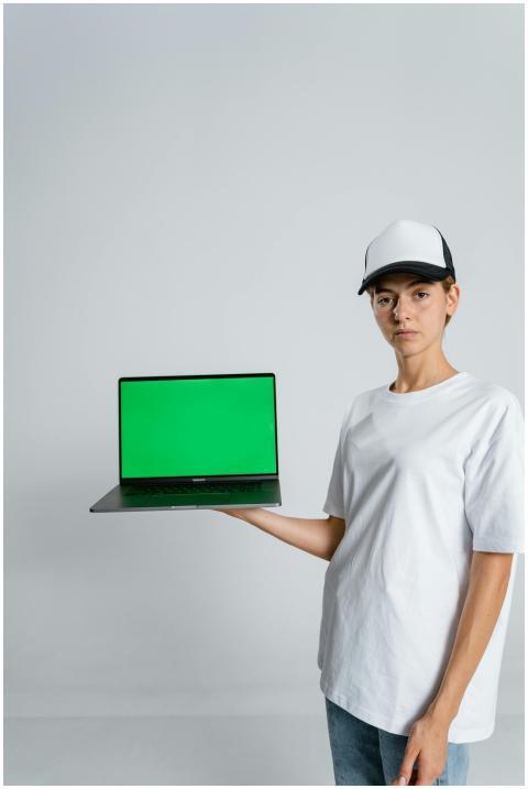 A woman in casual attire and cap holds a laptop wi