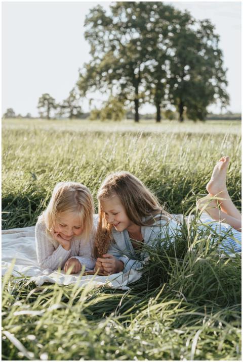 Two young girls reading a book on a blanket in a s