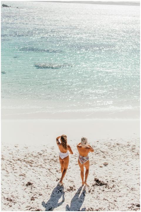 Two women in swimsuits walking on a sunny, sandy b