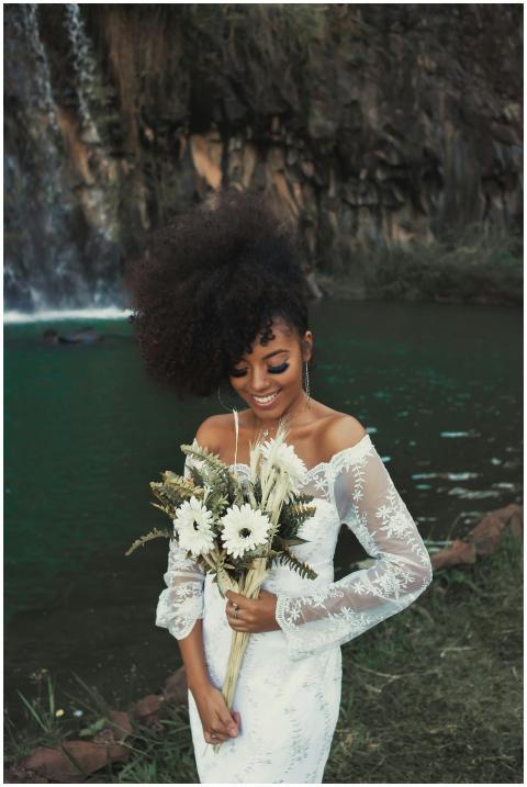Smiling bride with bridal bouquet by waterfall in
