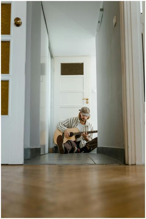 A young man sits in a hallway, playing guitar with