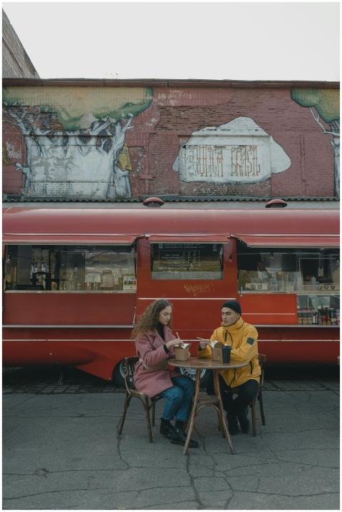 A couple dining near a bright red food truck on a
