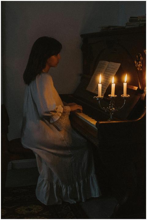 A woman elegantly plays the piano in a dimly lit r