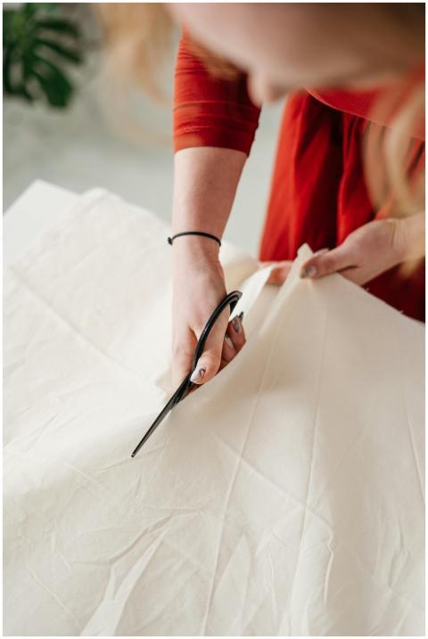 Focused seamstress cutting white cotton fabric wit