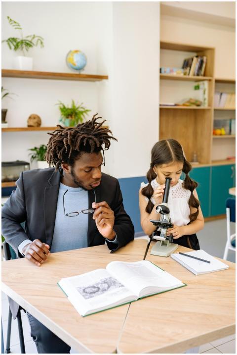 A teacher helps a young student use a microscope i