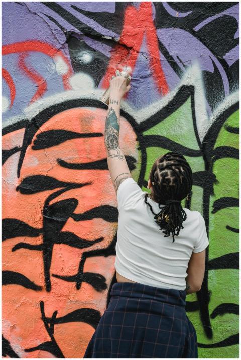 A woman with tattoos spray painting a vibrant graf