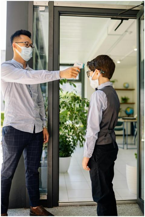 Masked school staff checks student's temperature f