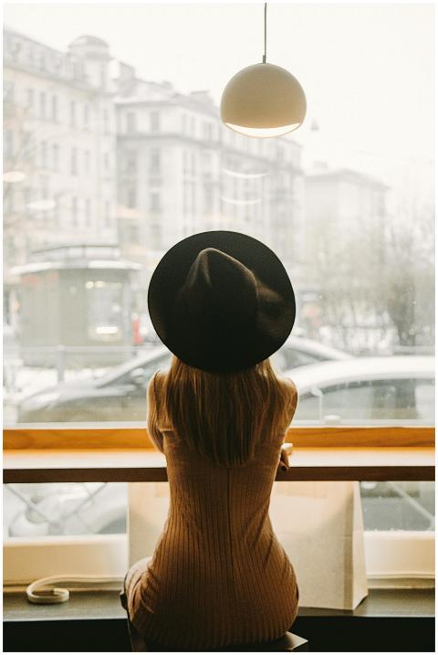 Stylish woman in a hat sits in a café, gazing outs