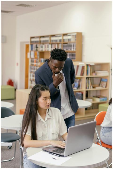 Teacher helping a student on a laptop in library c