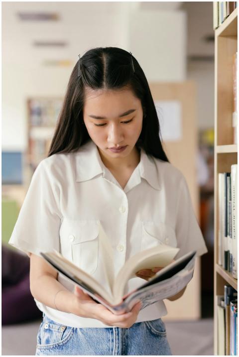 East Asian woman reading a book in a library. Perf