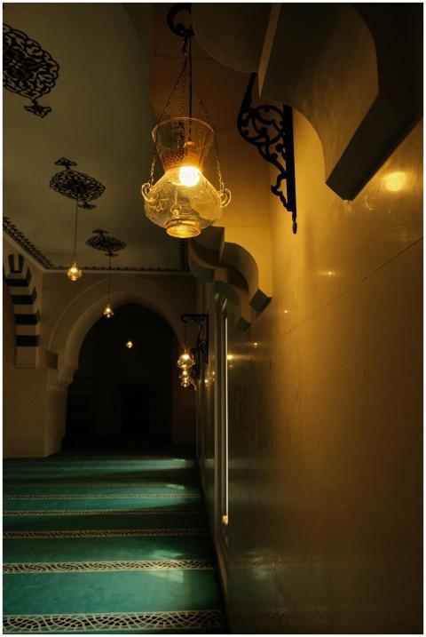 Warmly lit corridor inside a mosque, featuring ele