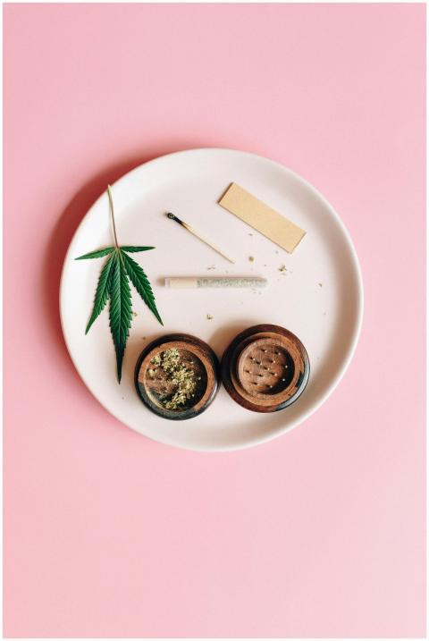 A cannabis leaf, grinder, and joint on a pink back