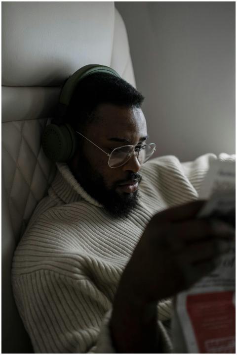 Man on a flight wearing headphones, reading a news
