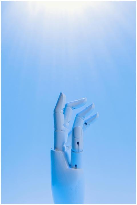 A robotic hand reaching upward against a blue sky,