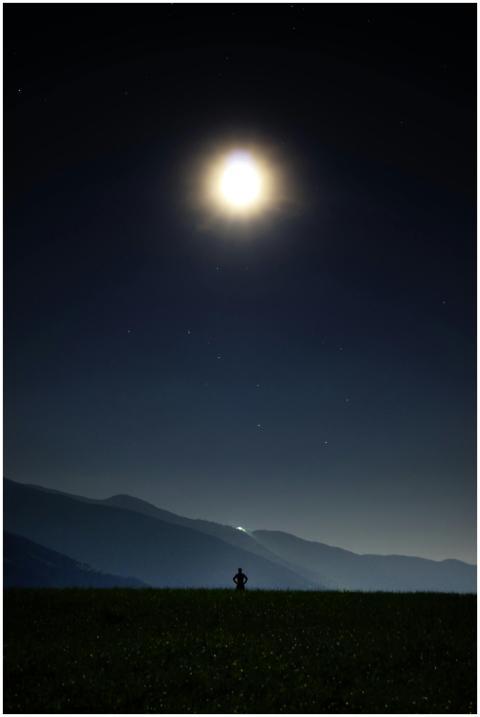 A person stands silhouetted against a moonlit nigh