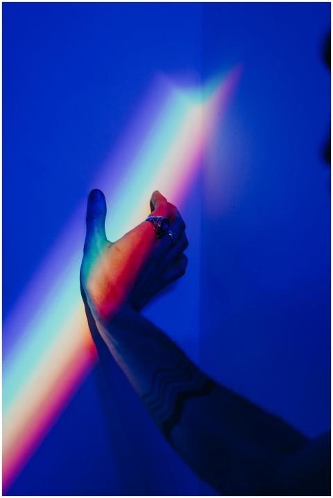 A tattooed hand reaches for vibrant rainbow light