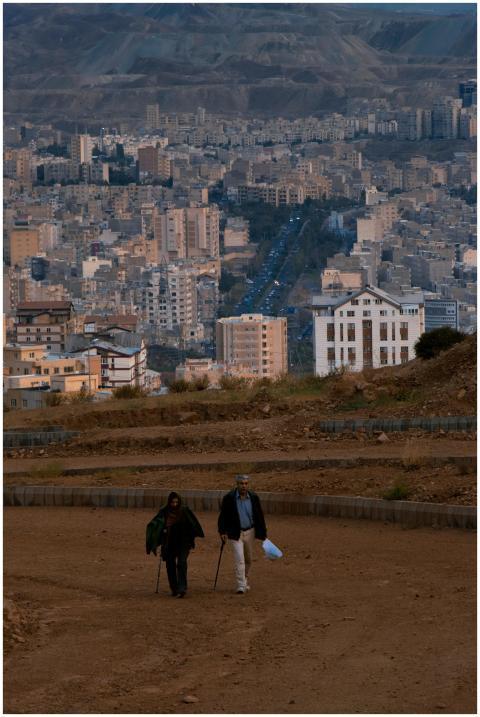 Two adults walking on a path with a cityscape back