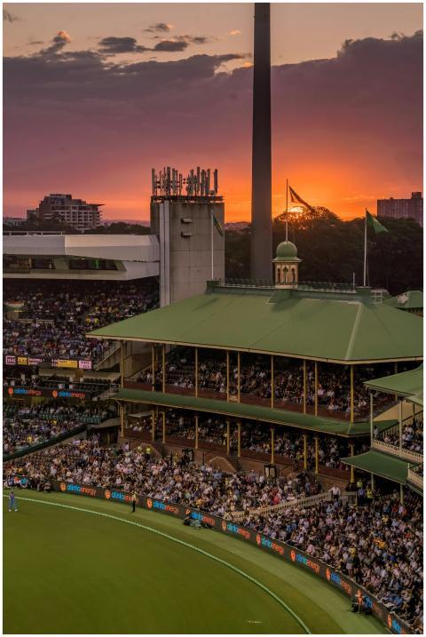 A colorful sunset over a bustling cricket stadium,