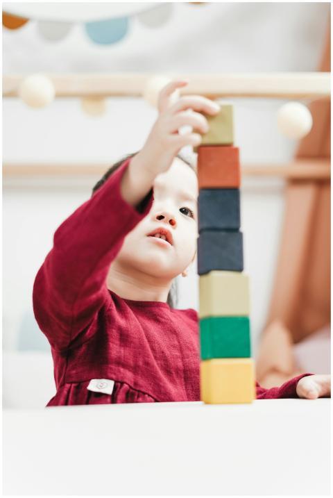 A young child in a red dress plays by stacking col