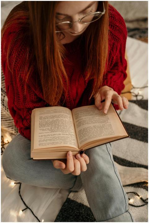 A young woman in a red sweater reads a book while