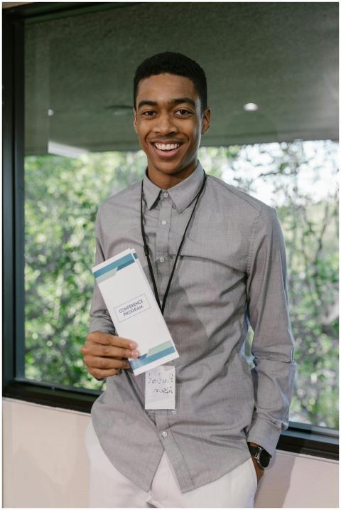 Smiling young man holding a conference program at