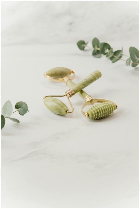 A jade roller set with green leaves on a marble su