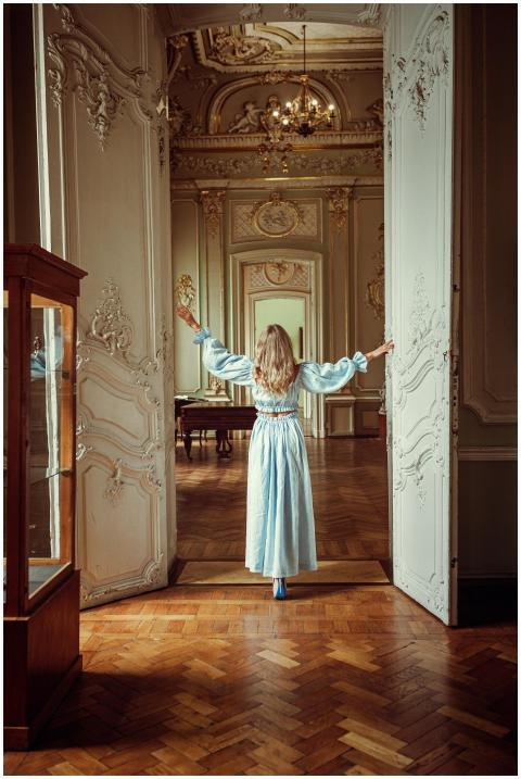 A woman in a light blue dress stands in an ornatel
