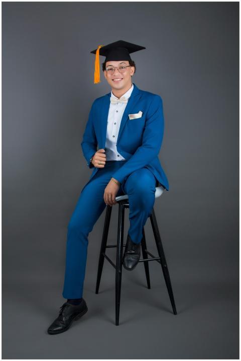 Young adult in blue suit and graduation cap poses
