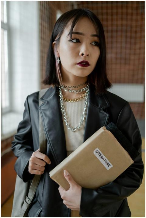 Asian student in black leather jacket holding a li