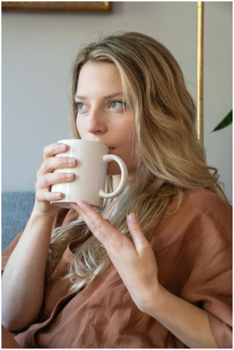 A woman with blonde hair sipping from a ceramic mu