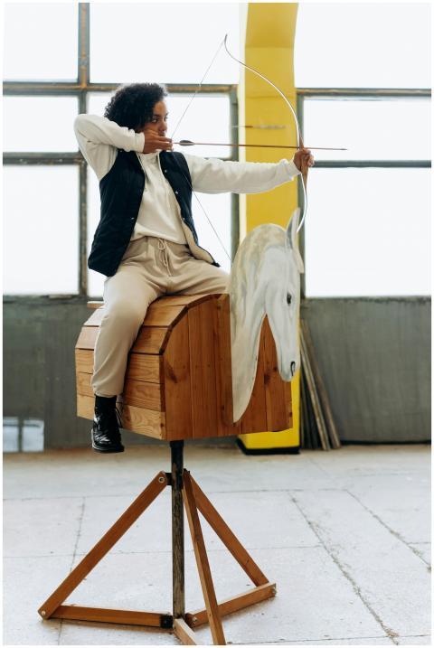 A young woman practicing archery indoors on a hors