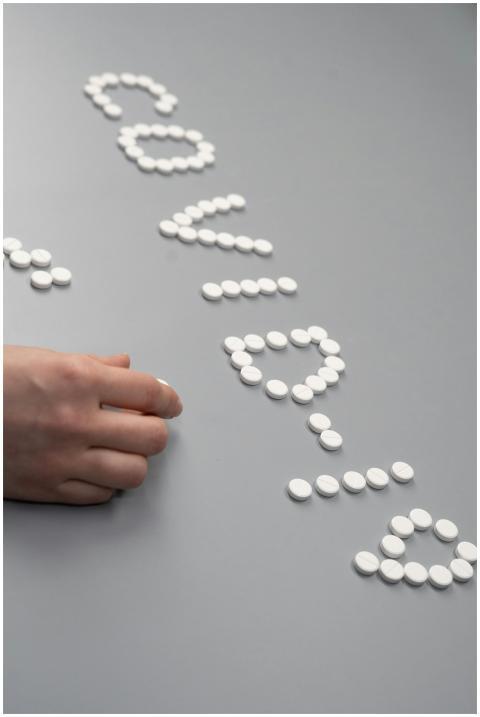 White pills arranged to spell 'COVID' on a gray ta