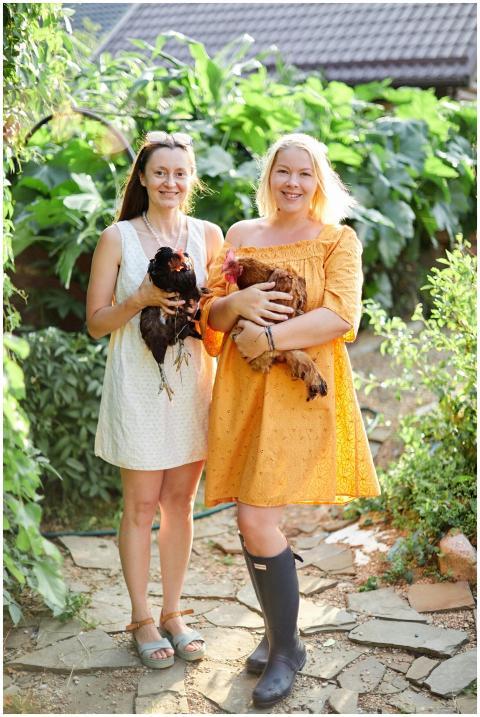Two women joyfully hold chickens in a lush, sunny
