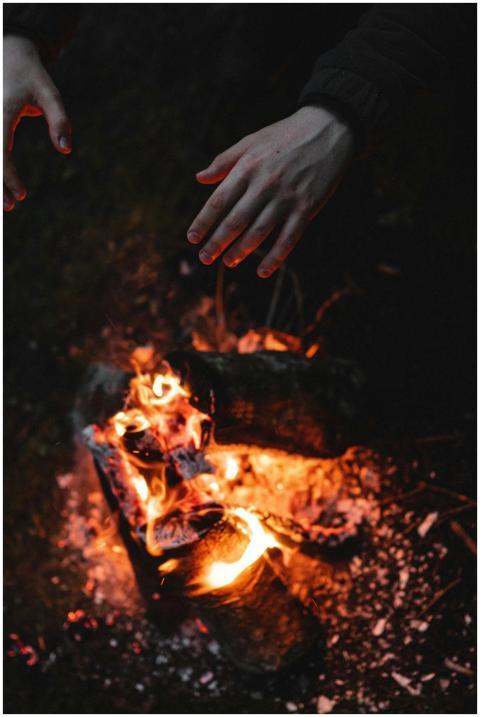 Close-up of hands reaching over a campfire, provid