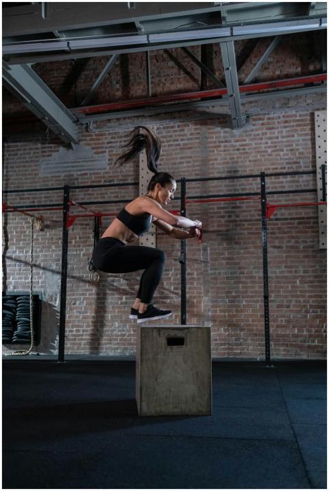A fit woman executes a box jump in a gym setting,