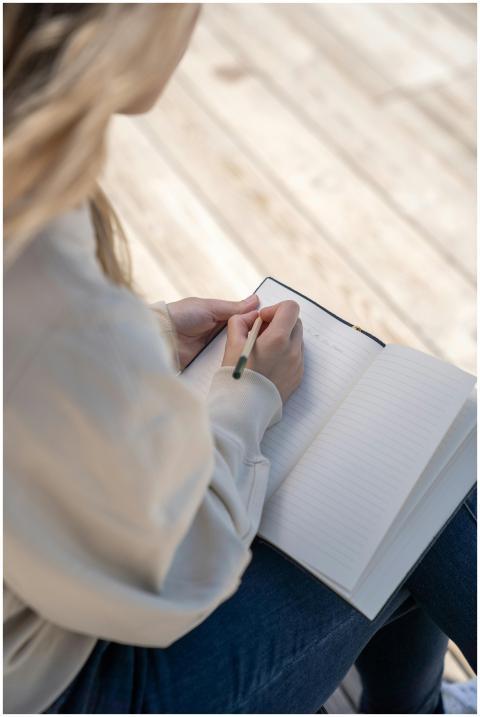 A woman sits indoors writing in a notebook, captur