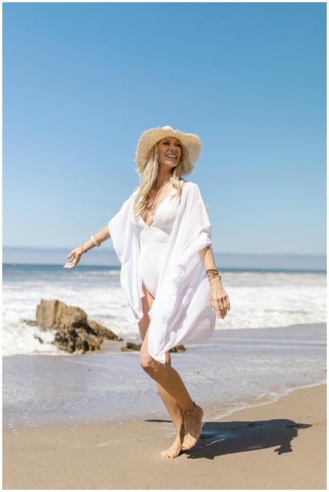 A smiling woman in a sun hat enjoys a walk on a su