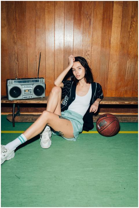 A young woman in casual attire sits against a wood