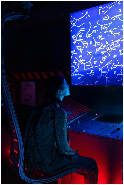 A woman in a space suit studies a futuristic contr