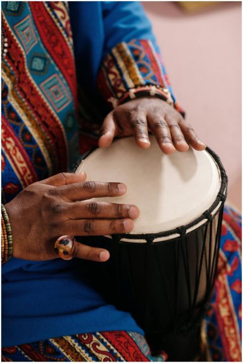 Hands playing a djembe drum, wearing colorful trad