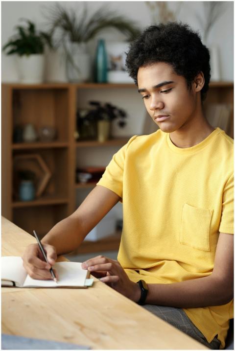 Focused teen boy studying at home in a yellow shir