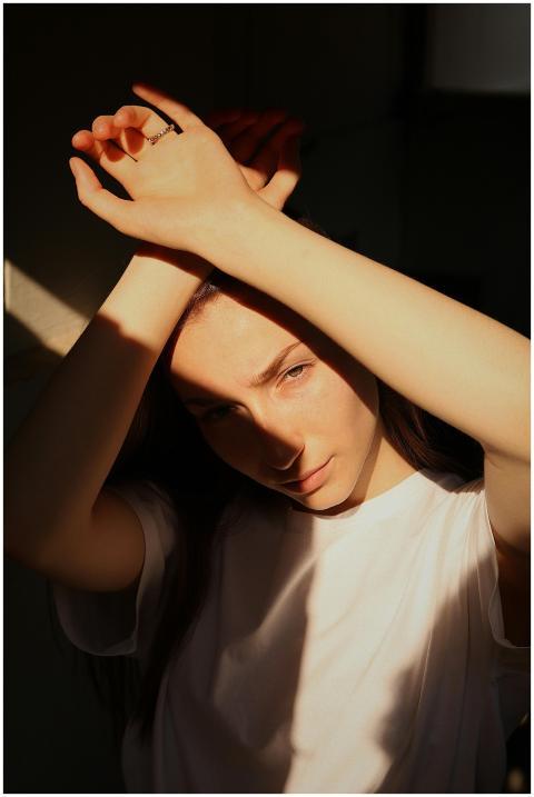 A young woman in a white shirt, hands raised, with
